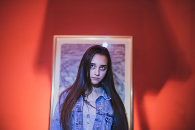 Young woman looking away while standing against picture frame and wall