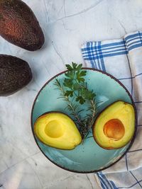 Fresh avocado with herbs and lemons lies on the table on blue plate on white background. flat lay