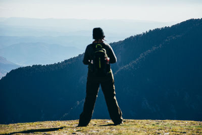Full length rear view of man with backpack standing on mountain against sky