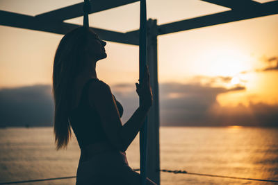 Side view of woman looking at sea against sky during sunset