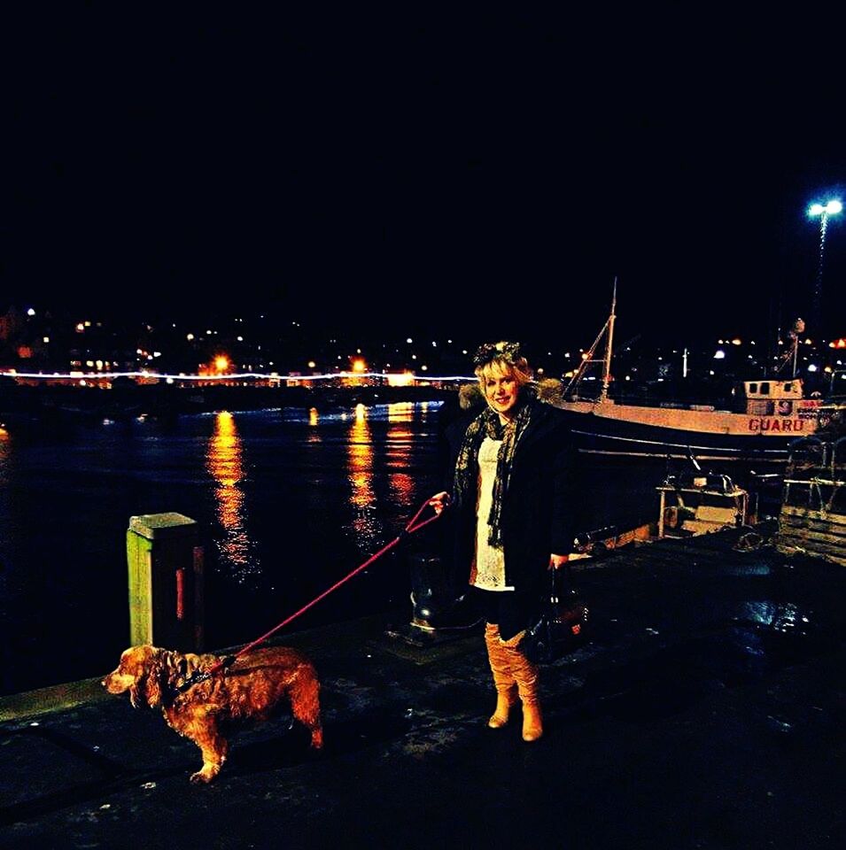 REAR VIEW OF MAN ON ILLUMINATED BRIDGE OVER RIVER IN CITY