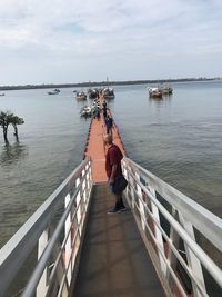 Rear view of man on pier over sea against sky