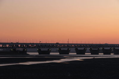 Bridge over sea against orange sky