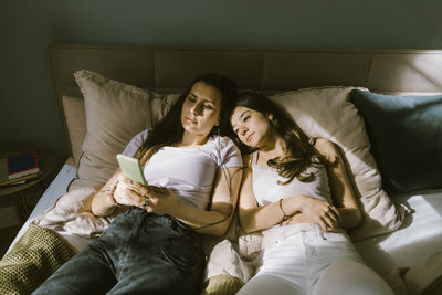 High angle view of young women sharing smart phone while lying on bed at home
