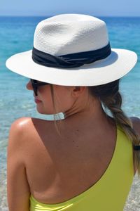 Rear view of woman wearing hat while sitting at beach