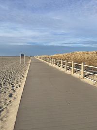 Footpath-boardwalk leading towards beach against sky