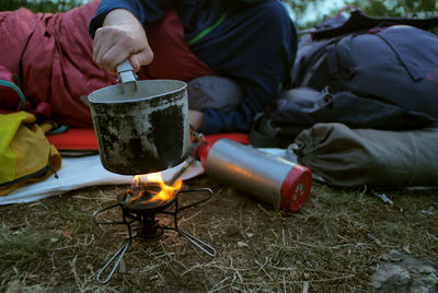 Female hiker making drink while leaning on bed at field during camping