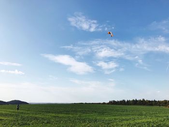 Distant view of man paragliding from field against sky