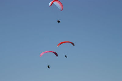 Low angle view of people paragliding against clear blue sky