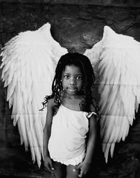 Portrait of girl standing against wall with wings