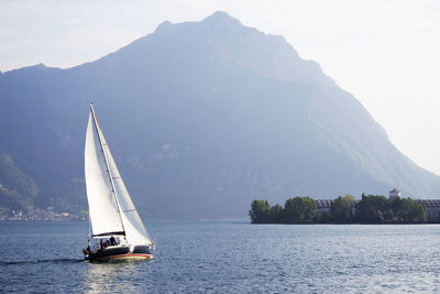 Sailboat sailing on sea by mountain against sky