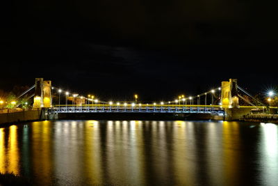 Illuminated bridge over river against sky at night