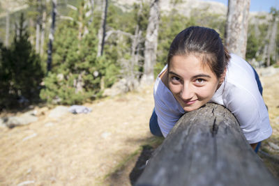 Portrait of young woman lying on tree trunk in forest