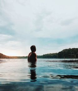 Shirtless man in lake against cloudy sky