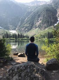 Rear view of man sitting on rock by lake in forest