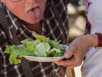 Cropped image of woman holding salad in plate while man sticking out tongue