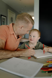 Father assisting son with down syndrome in studying at dining table