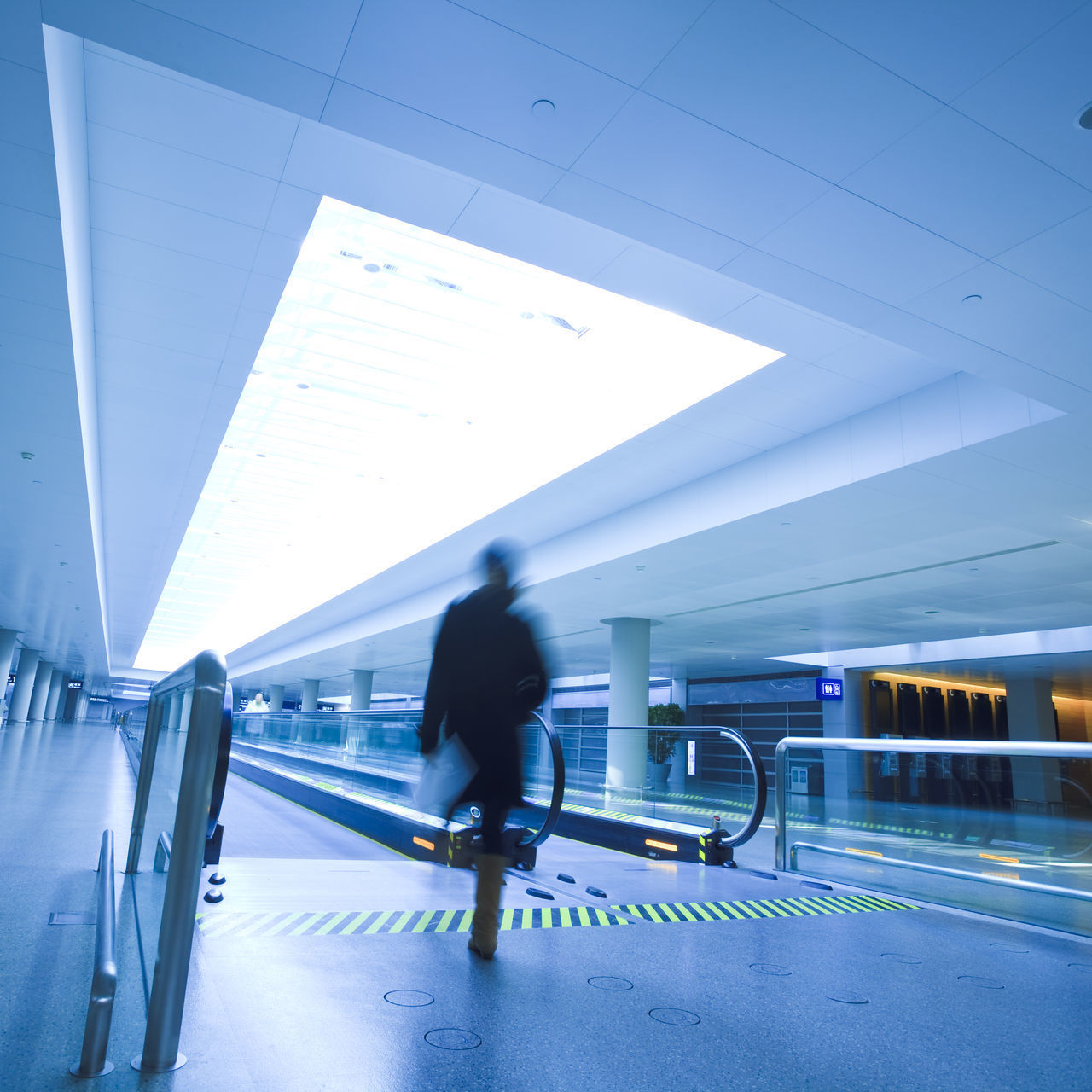 REAR VIEW OF MAN WALKING ON ILLUMINATED RAILROAD STATION