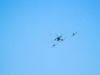 Low angle view of air vehicles flying against clear blue sky