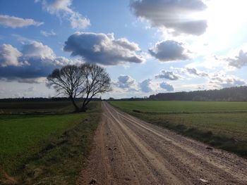 Dirt road amidst field against sky