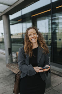Portrait of happy female commuter standing at railroad station