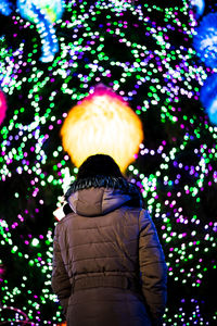 Rear view of woman standing against multi colored lights