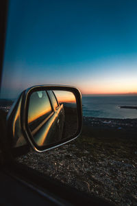 Reflection on side-view mirror at beach against sky during sunset