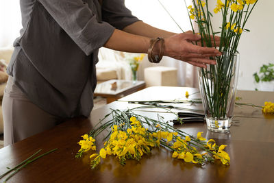 Midsection of woman with yellow flowers in vase on table