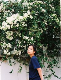 Portrait of young woman standing by flowering tree