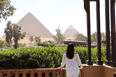 Rear view of woman standing by building against sky