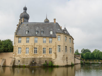 Old building by river against cloudy sky