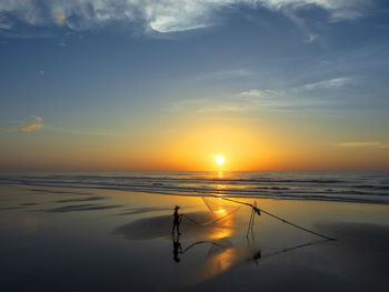 Fisherman working with net at beach during sunset