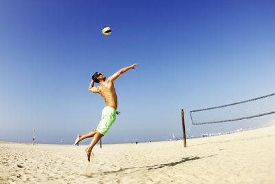 Man hitting ball at beach against clear sky