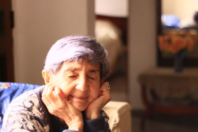 Close-up of senior woman with hands on chin and eyes closed sitting at home