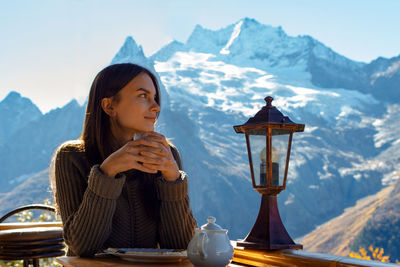 Young woman drinking coffee on street against mountains during winter