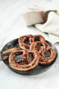 German brezel pretzel with sesame seed on rustic plate, marble white background