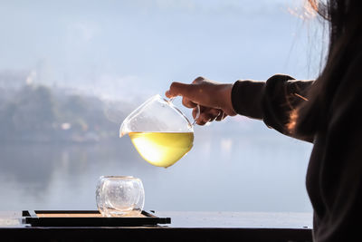 Female hands pouring hot tea with lake background at sunrise.