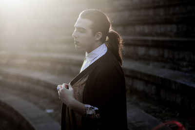 Side view of young woman standing against built structure