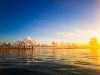 Silhouette people on sea against sky during sunset