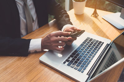 Midsection of businessman using phone by laptop on table