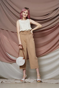Portrait of smiling young woman standing against wall