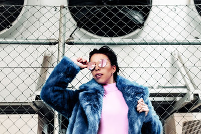 Smiling woman wearing sunglasses against chainlink fence during winter