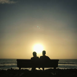 Silhouette people sitting on bench at beach during sunset