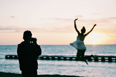 People at sea shore against sky during sunset