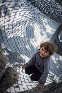 High angle portrait of boy smiling while sitting on net