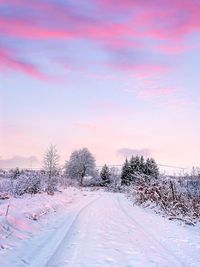 Road on snow covered field against sky during sunset