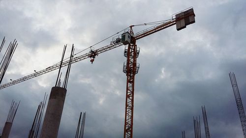 Low angle view of cranes against cloudy sky