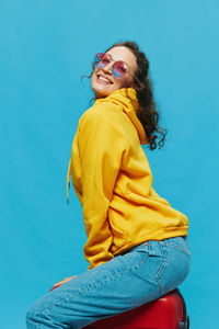 Young woman wearing sunglasses while standing against blue background