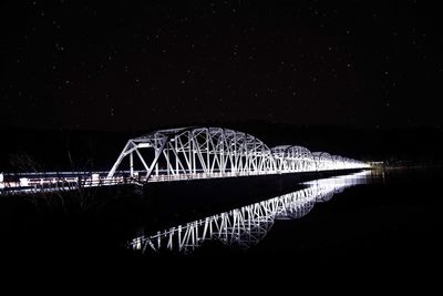 Illuminated bridge over river against sky in city at night