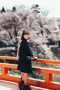 Side view of woman standing by railing against trees